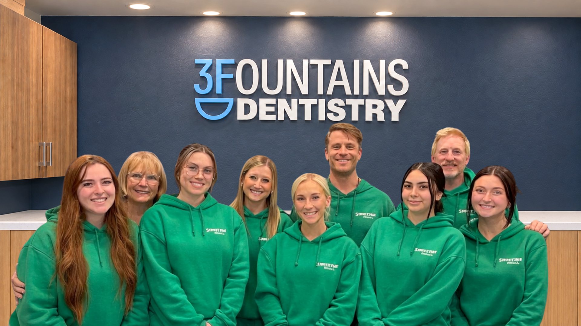 The Three Fountains Dentistry team in green hoodies in front of the 3 Fountains Dentistry sign